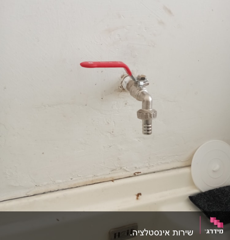 ברז עם ידית אדומה על קיר לבן